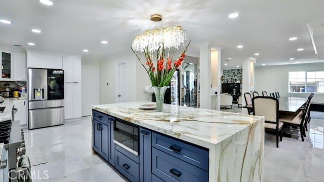 Kitchen with a blue island, marble countertop, and white tile flooring open to a dining area